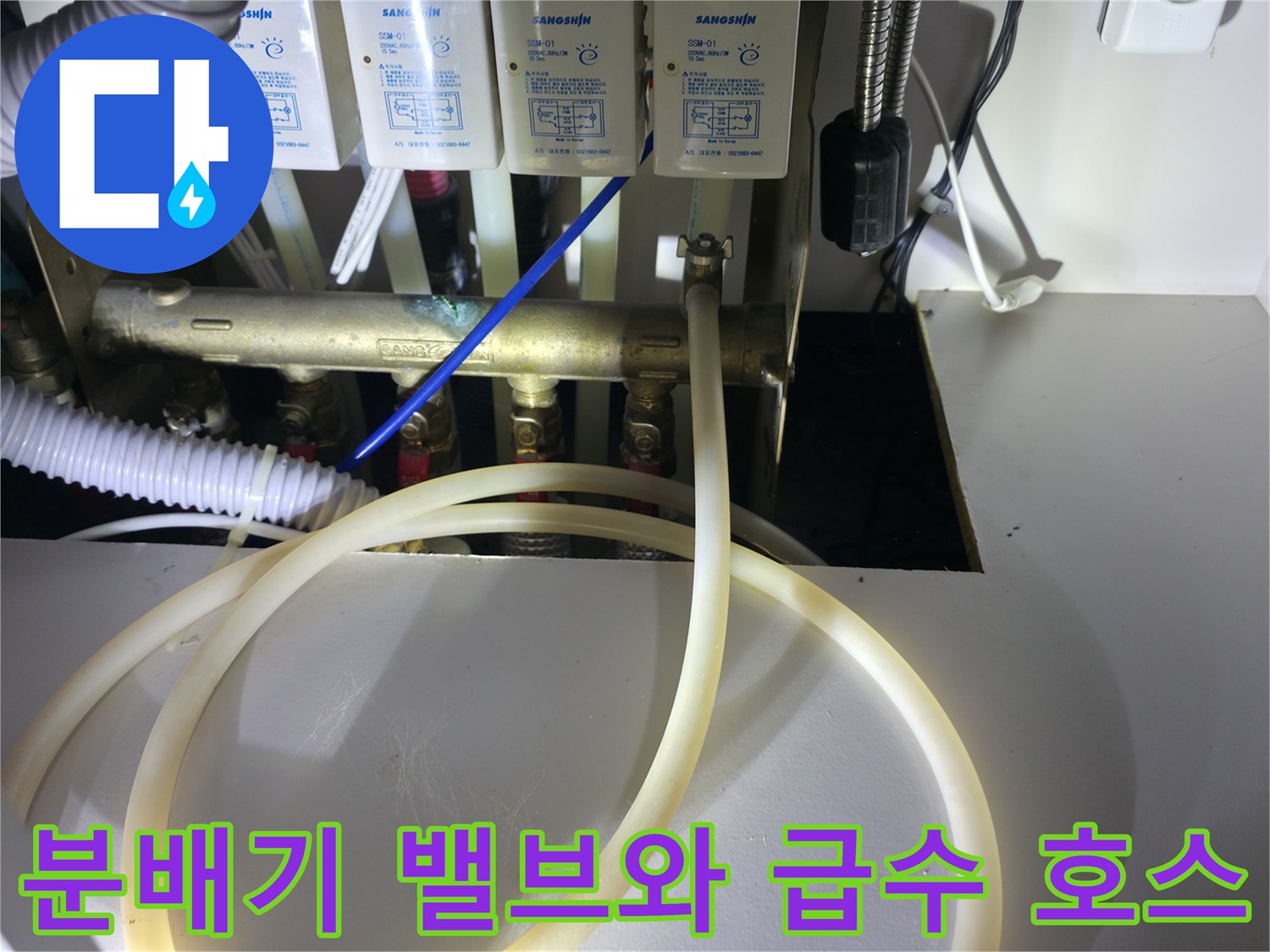 싱크대 하부의 금속 분배기 밸브와 흰색 연결 호스