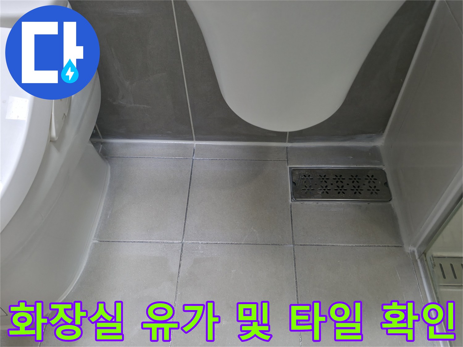 하얀색 변기 옆 바닥의 배수구와 타일 접합부 모습입니다.