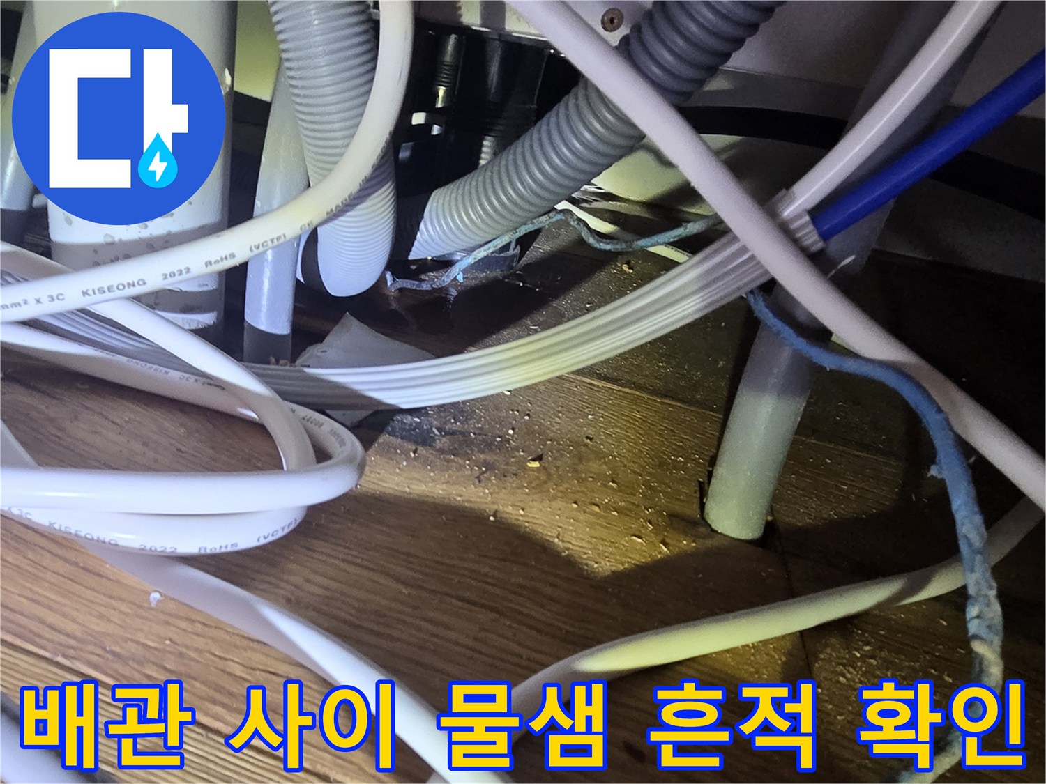 싱크대 하단 복잡한 배관 주변의 젖은 바닥재 모습