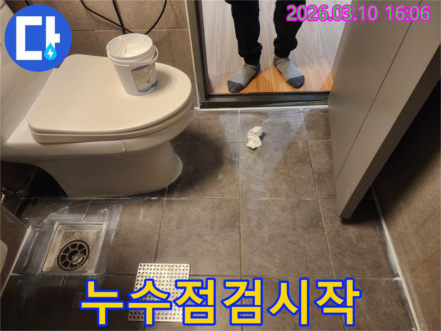 욕실 바닥 타일에서 누수 흔적을 확인하는 모습입니다- 변기 주변과 배수구 근처를 꼼꼼히 점검하고 있습니다.