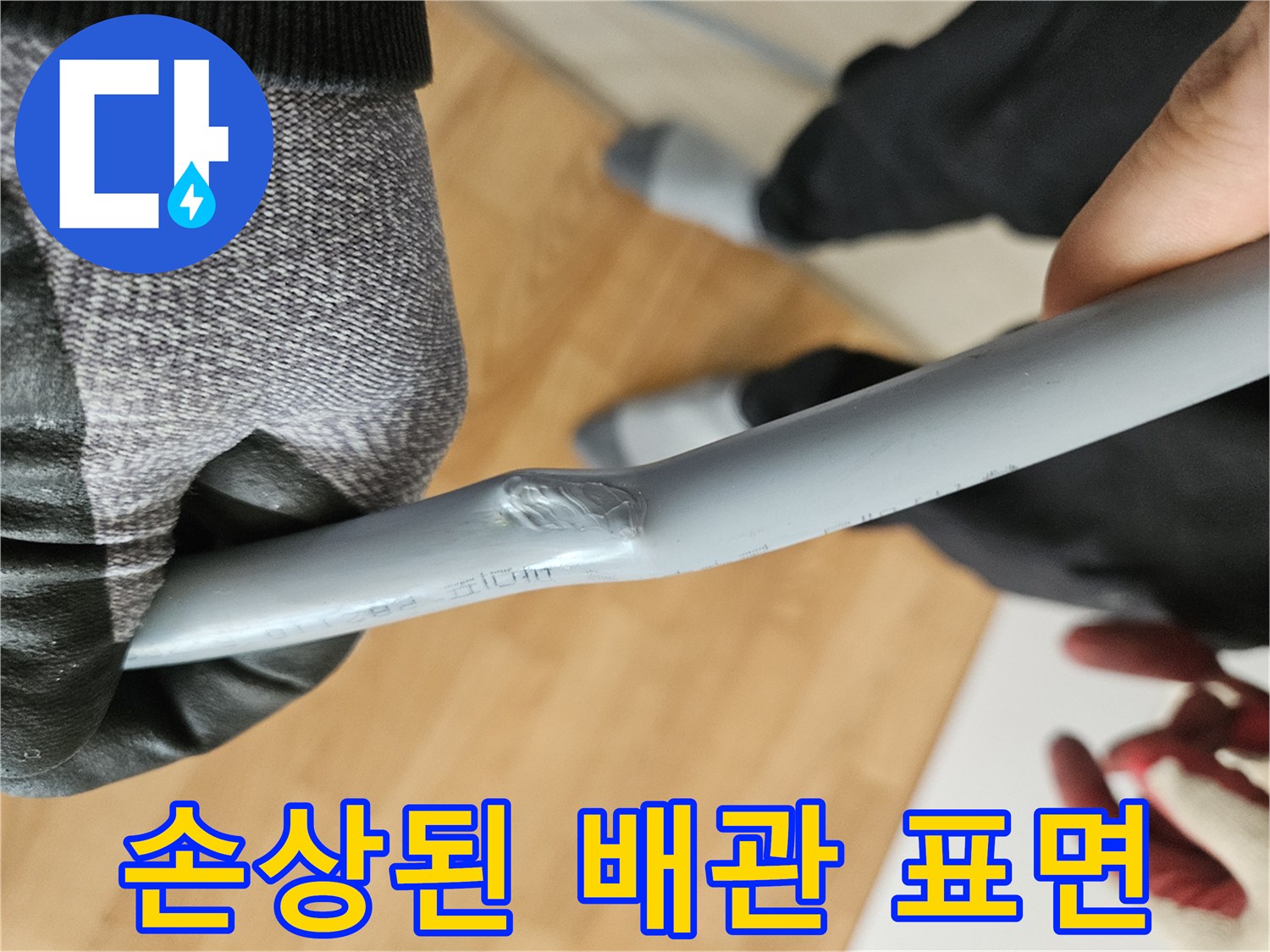 장갑을 낀 작업자가 확인 중인 찌그러진 배관 부위