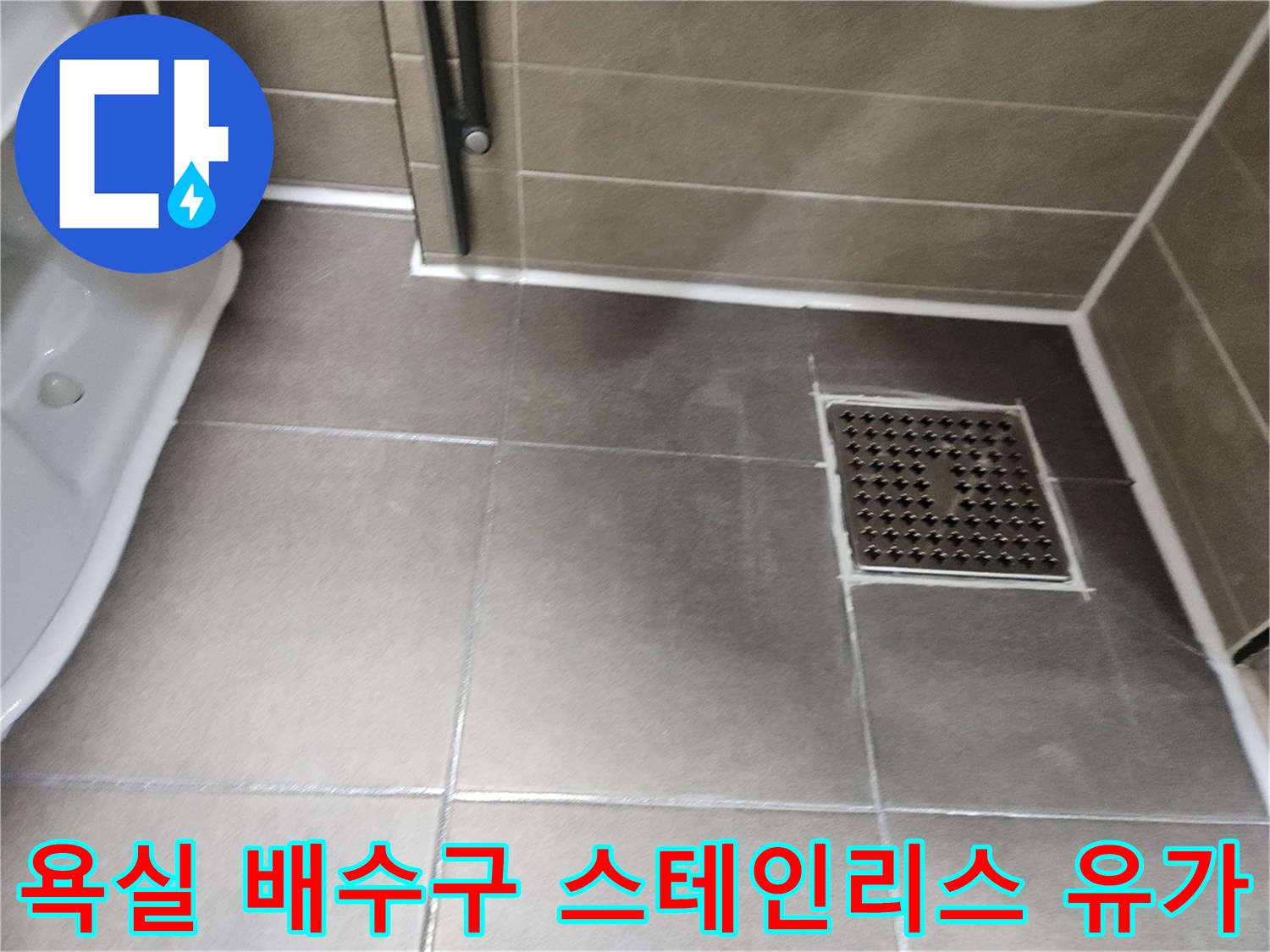 회색 타일 바닥에 설치된 스테인리스 재질의 배수구 덮개