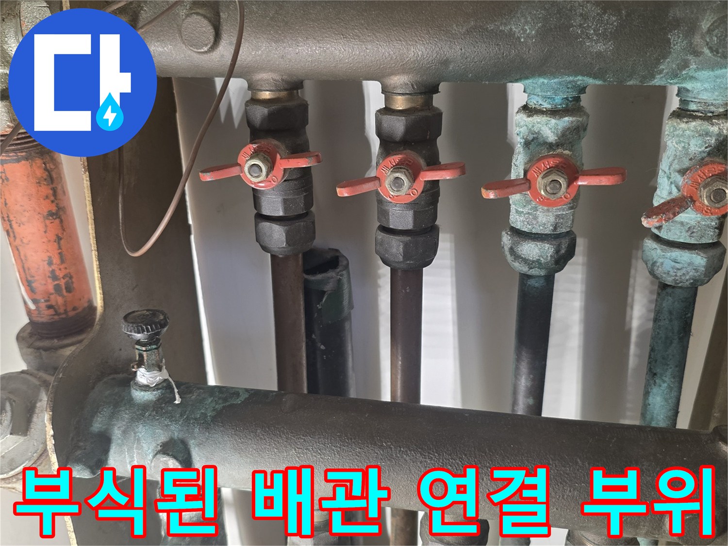 붉은색 밸브와 푸른 녹이 섞여 있는 배관 연결 구조
