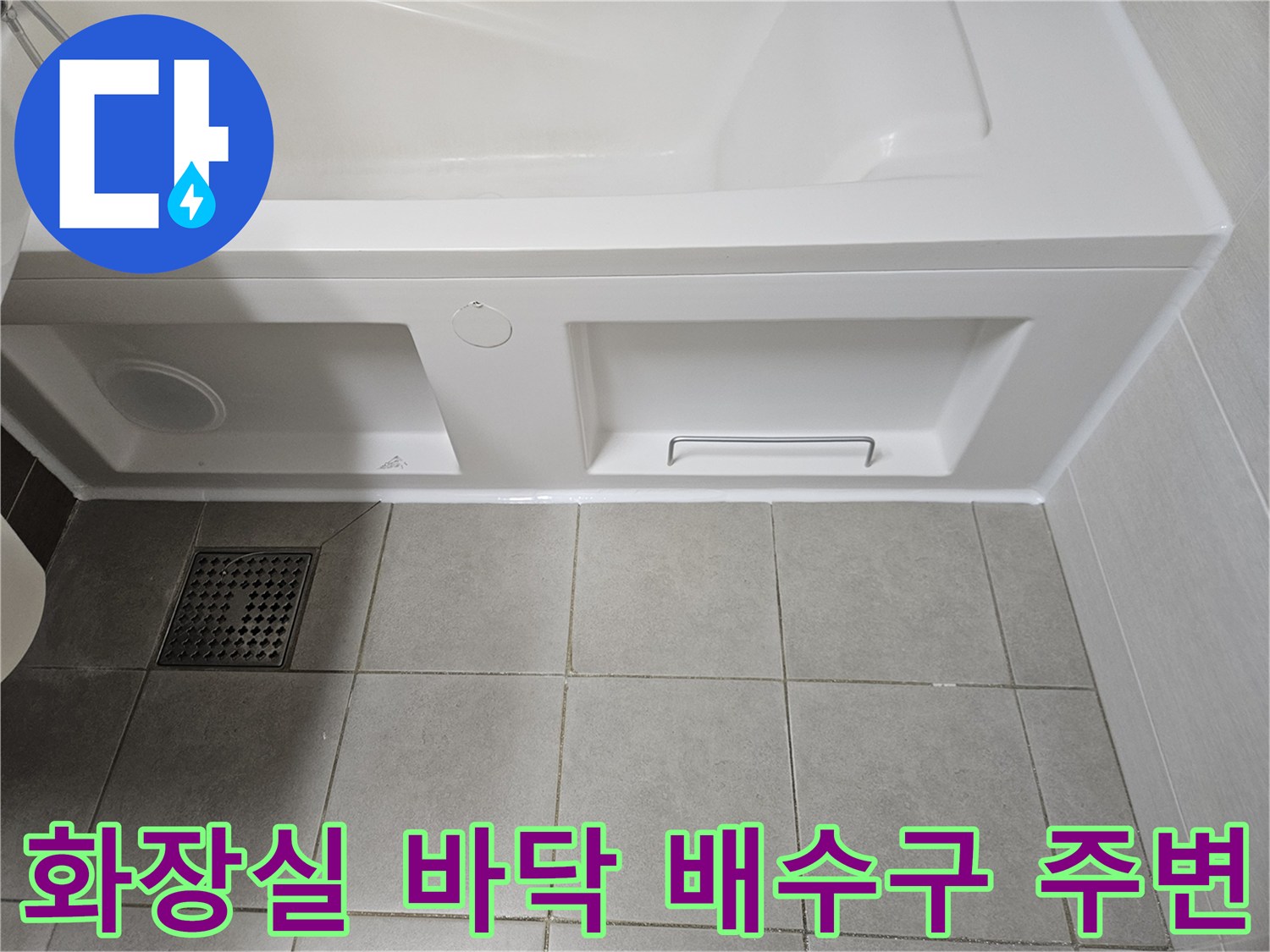 욕조 하단 패널 아래의 화장실 배수구와 타일 모습입니다.
